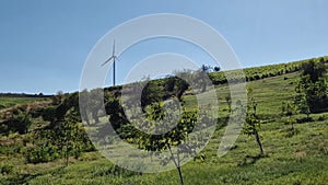 Wind turbine on the top of a hill over the country valley with vineyard and fruit trees