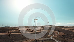 Wind turbines aerial, empty desert road, yellow hill. Cinematic drone view of large windmills blades