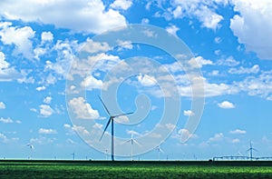 Wind turbines in agricultural field on Plains under beautiful blue cloudy sky with irrigation equipment in distance - selective