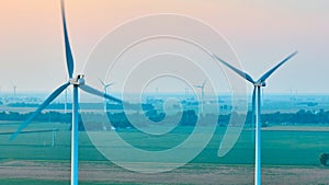 Wind turbines caught in motion on hazy morning with soft pink sky aerial