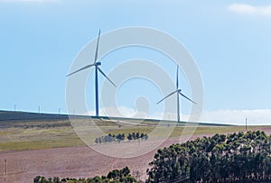 Wind turbines with clouds in the background and trees in the foreground.