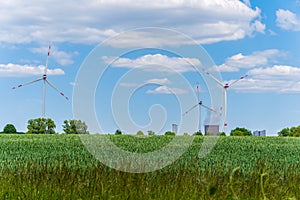 Wind turbines and electric power plant with smoking chimney in beautiful landscape with lush green agricultural wheat field.