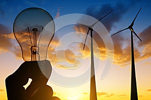Wind turbines and electrical light bulb in hand.