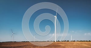 Wind turbines on field. Empty field in foreground, blue sky on background.