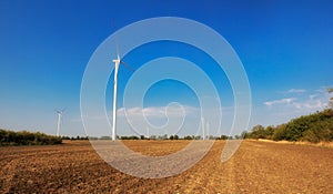 Wind turbines on field. Empty field in foreground, blue sky on background.