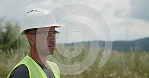 Wind turbines generate alternative energy under clear sky. Technician in orange helmet stands against rotating