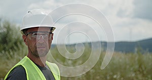 Wind turbines generate alternative energy under clear sky. Technician in orange helmet stands against rotating