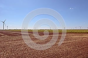 Wind turbines generating electricity on the foreground plowed field. The concept of alternative green energy