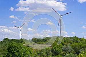 Wind turbines in a green field against a blue sky with clouds.