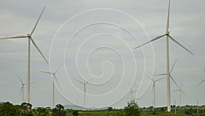 Wind turbines in the green field are rotating with overcast