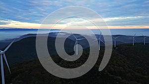 Wind turbines in the mountains during sunrise and thick morning fog in the valley. Wind farm producing green energy.