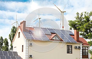 Wind turbines near house with installed solar panels. Alternative energy source