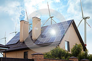 Wind turbines near house with installed solar panels. Alternative energy source