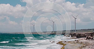 Wind turbines spinning along rocky beach with ocean waves in Curacao, Caribbean