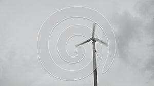 Wind turbines are spinning on cloudy sky background in rainy season. Green energy generation.
