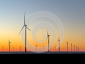 Wind turbines at sunset. Offshore wind mills, wind farm, generating electricity, rotating at orange sunrise