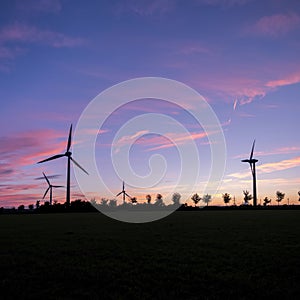 Wind turbines and trees form silhouettes against colorful sunset