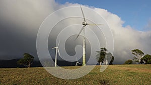 Wind turbines turning in the sunshine while a storm brews in the background