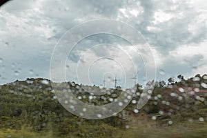 Wind turbines under a cloudy sky seen through the wet glass window of the car