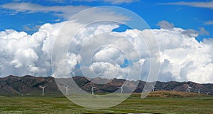 Wind turbines Or Windmills On Green Grass Fields With Mountain Ranges And Cloudy Blue Sky Background