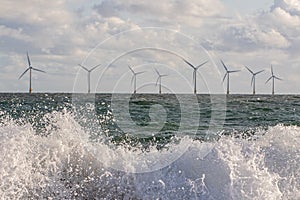 Wind and wave energy. Breaking waves with offshore windfarm turbines background