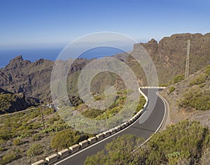 Winding asfalt road to village Masca with green hills, sharp mountain peaks, sea horizon clear blue sky background photo