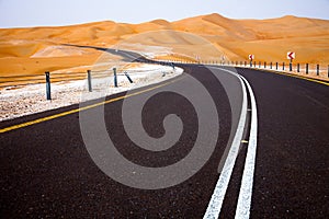 Winding black asphalt road through the sand dunes of Liwa oasis, United Arab Emirates