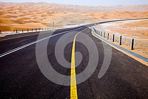 Winding black asphalt road through the sand dunes of Liwa oasis, United Arab Emirates