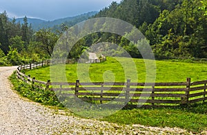 Winding country road with old wooden fence and green meadow