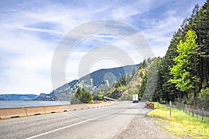 Winding highway road along the Columbia River with big rig semi truck and dry van semi trailer and another traffic in Columbia