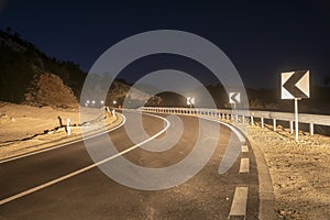 A winding mountain road at night illuminated by car headlights