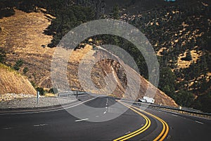 Winding Mountain road with white truck towing travel trailer in the distance climbing the incline