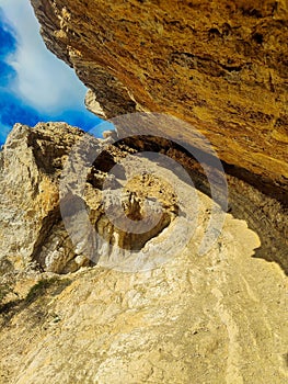 Winding mountain trail with large rock formations and a small cave entrance at the bottom