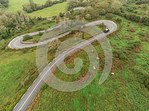 Winding narrow road on a hill in Burren, Ireland. Aerial drone view. Green fields and small trees around the pass