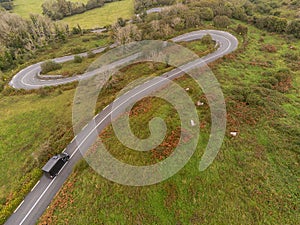 Winding narrow road on a hill in Burren, Ireland. Aerial drone view. Green fields and small trees around the pass