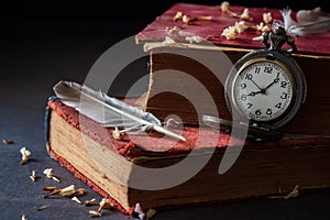 Winding pocket watch on old books with feathers and dried flower petals.