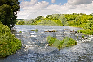 Winding river on a riffle in a summer forest in cloudy weather with rain clouds. Landscape in the river forest