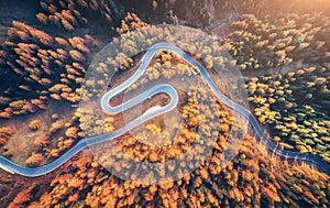 Winding road in autumn forest at sunset in mountains. Aerial vie