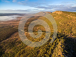 Winding road below rugged cliffs and low morning clouds.