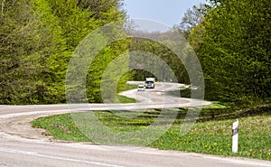 A winding road in the forest. A car and truck on a winding road in a forest