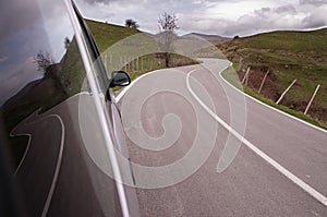 Winding road is reflected on side glass of a car