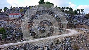 The winding road between the rocky mountains. House with red roof on a mountain slope with rock formations.