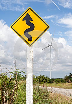 Winding road sign with windmill background in wind farm.