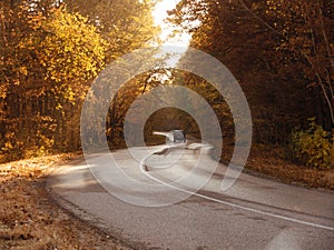 Winding rual road inside colorful autumn forest with black car