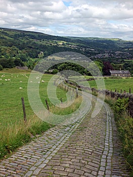 Winding stone cobbled lane running downhill in yorkshire landscape