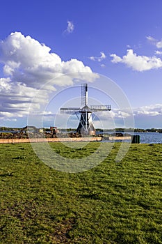 Windmill by the canal at Glimmen in Holland. Around the mills are excavators and the background is a blue sunny sky with white
