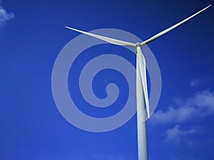 Windmill close up on blue sky and white cloud background. Wind-turbine on wind farm in rotation to generate electricity energy on