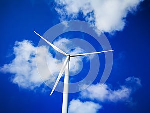 Windmill close up on blue sky and white cloud background. Wind-turbine on wind farm in rotation to generate electricity energy on