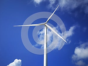 Windmill close up on blue sky and white cloud background. Wind-turbine on wind farm in rotation to generate electricity energy on