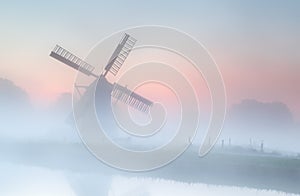 Windmill in dense fog at summer sunrise